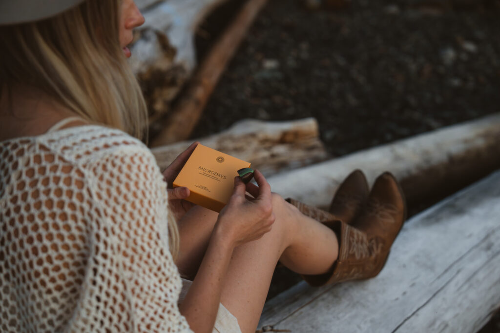 Woman sitting on a log in the forest holding a MicroDays box